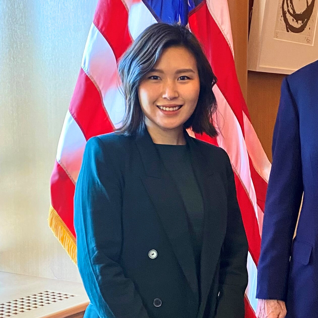 Grace Yoo stands in front of an American flag, smiling
