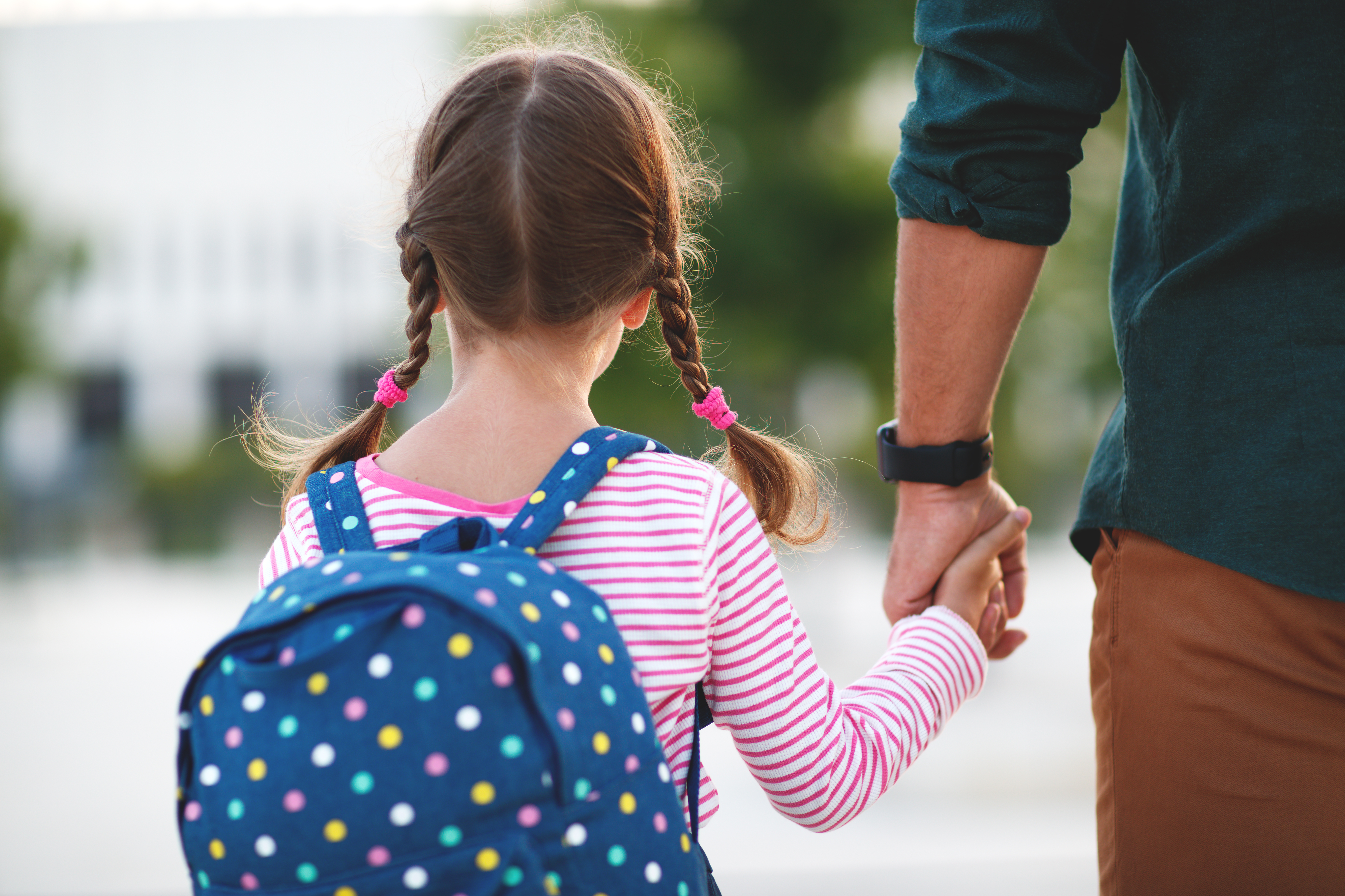 Young girl wearing a backpack holding her father's hand.
