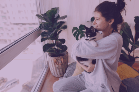 Young woman holds her cat in her arms and looks out the window.