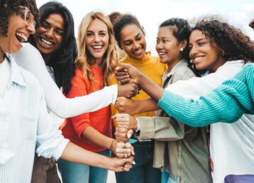 Group of women smiling and stacking their hands on top of eachother.
