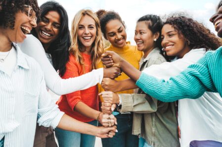Group of women smiling and stacking their hands on top of eachother.