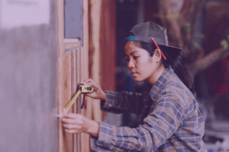Woman construction Carpenter uses measuring tape on wall.