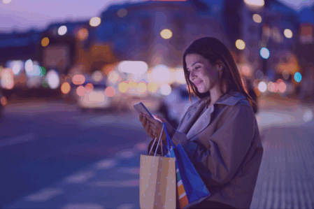 Woman smiles at phone at night. Lights are blurred in the bacgkground.